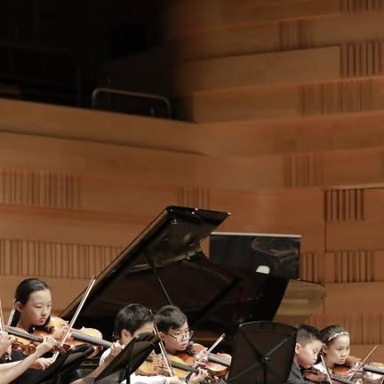 Young violinists and pianists perform with an orchestra.