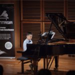 A young student in a bow tie performing on a Steinway concert grand at a Fantasia student concert.