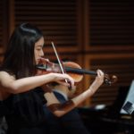 An advanced violin student performing with piano accompaniment in the concert hall.