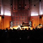 A full concert hall watching a student perform at the grand piano, Fantasia banners either side of the stage.