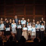 Students holding award certificates on stage with their teachers after a Fantasia concert.