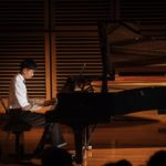 A teenage student performing on the Steinway concert grand under a spotlight.